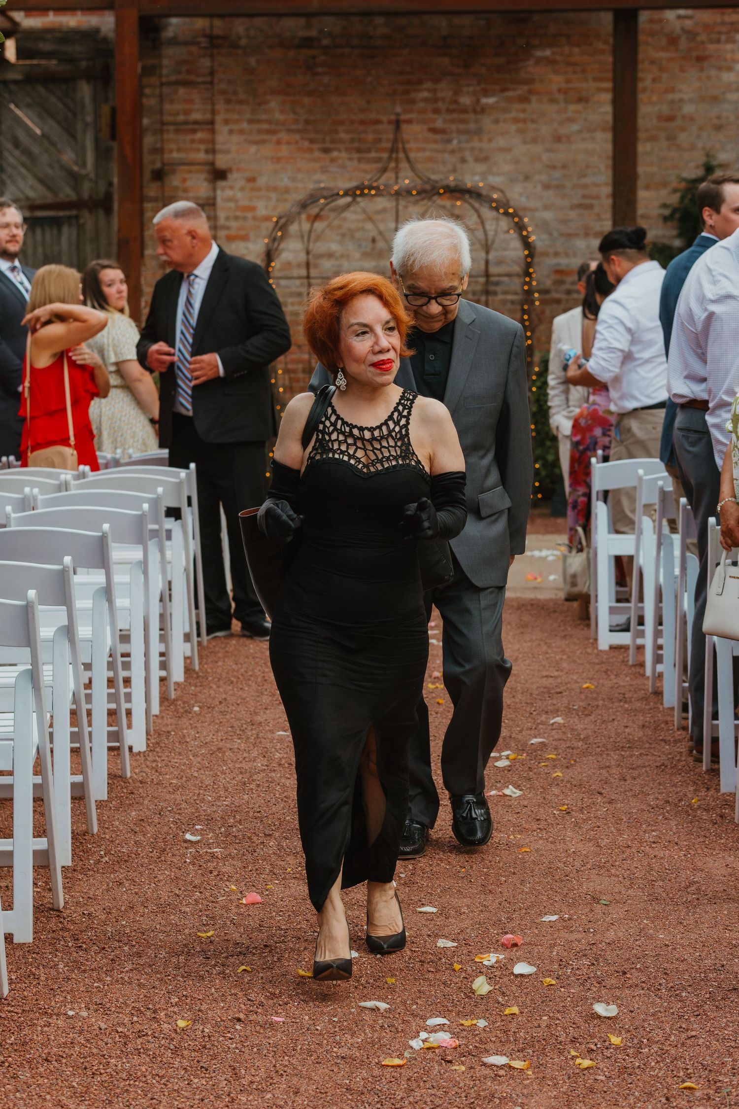 An elegant woman in a black gown walks down a wedding aisle escorted by a man in a suit. Chicagoland wedding venues.
