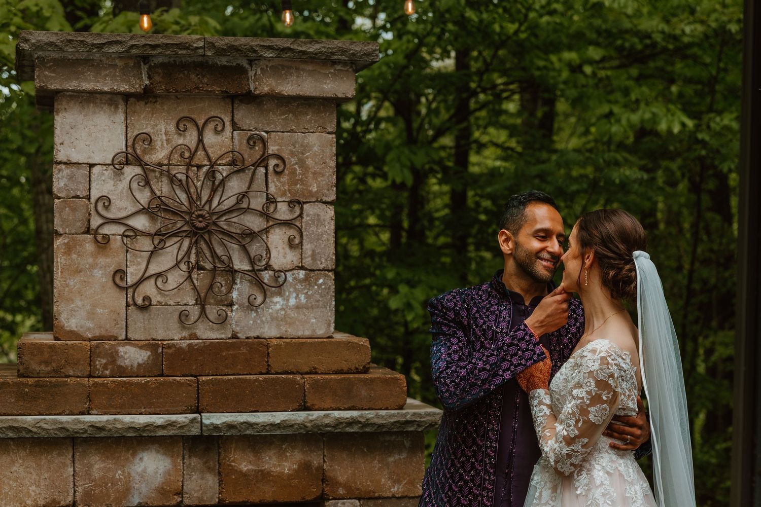 Couple shares tender moment by stone monument surrounded by lush green forest. Documentary style wedding photos.