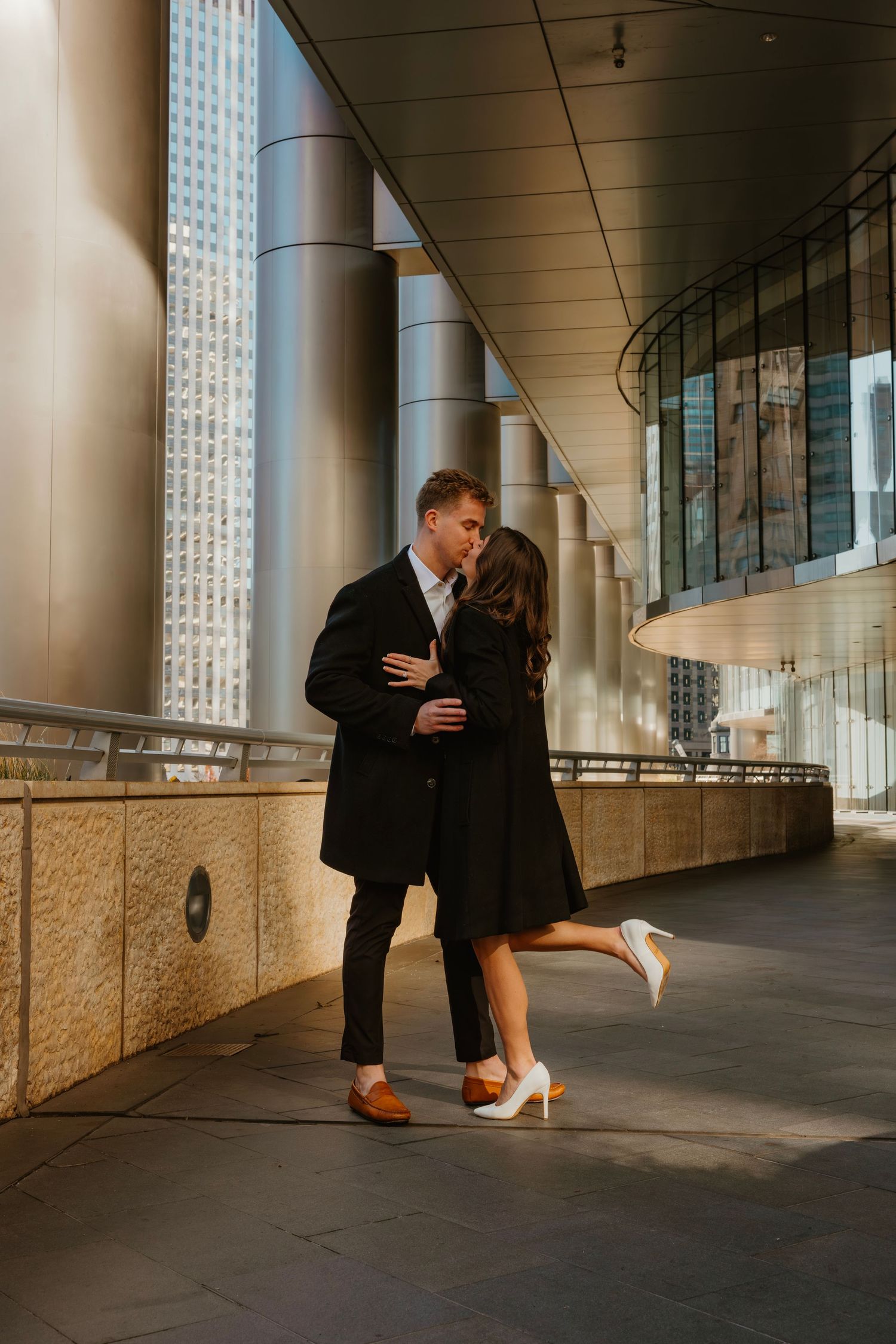 Couple sharing romantic kiss in urban corridor with dramatic architectural columns. Outdoor Chicago engagement photos.