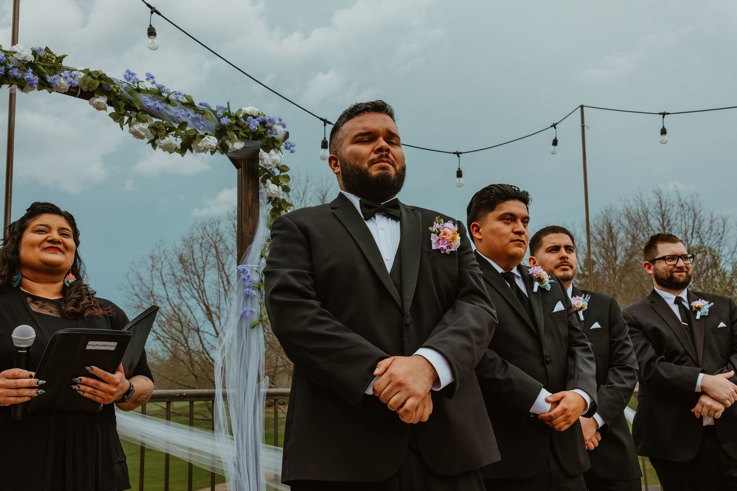 Groom in black tuxedo standing at outdoor wedding altar with groomsmen behind him. Chicagoland wedding venues.