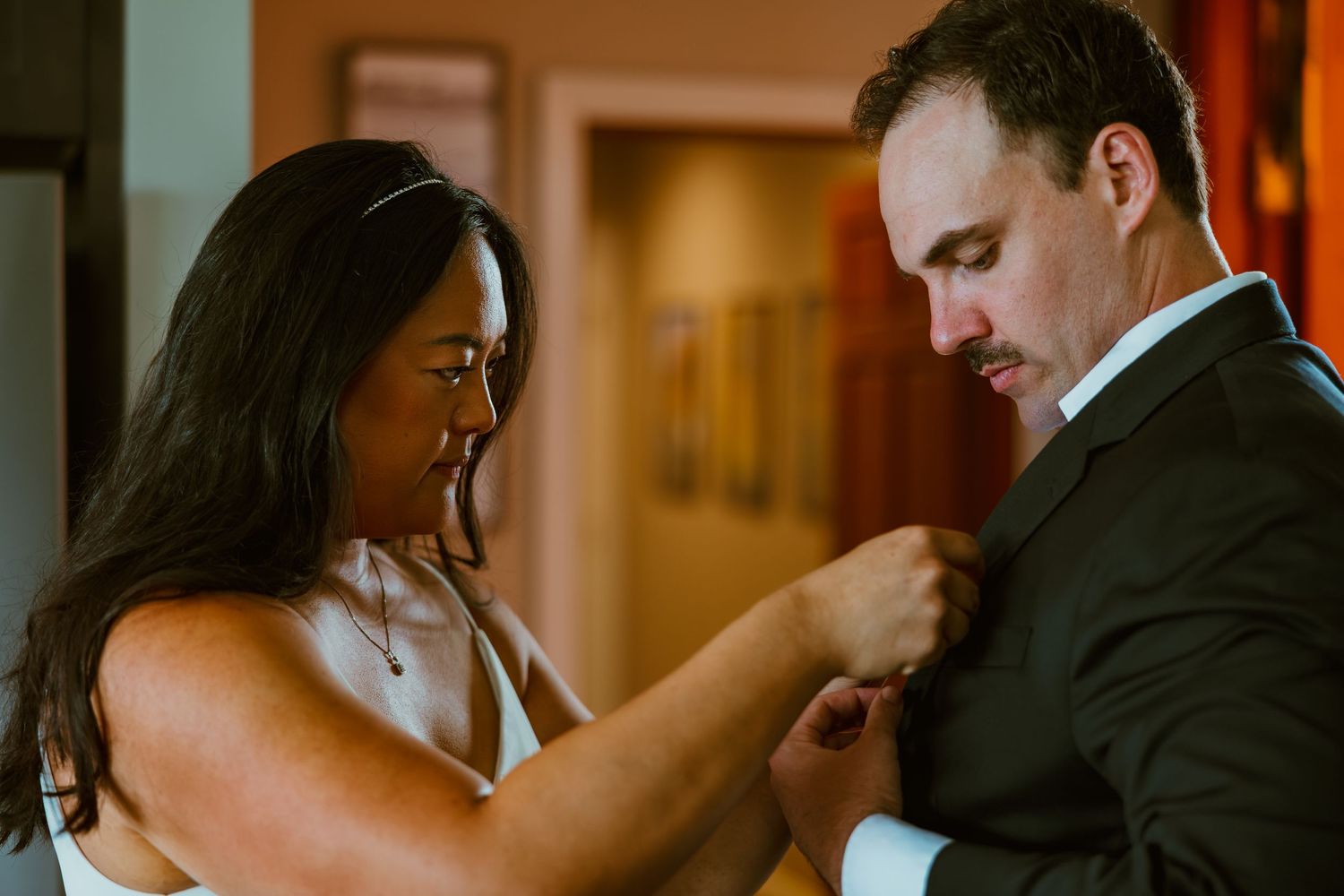 Woman helping groom with his boutonniere while preparing for wedding ceremony indoors. Michigan elopement.