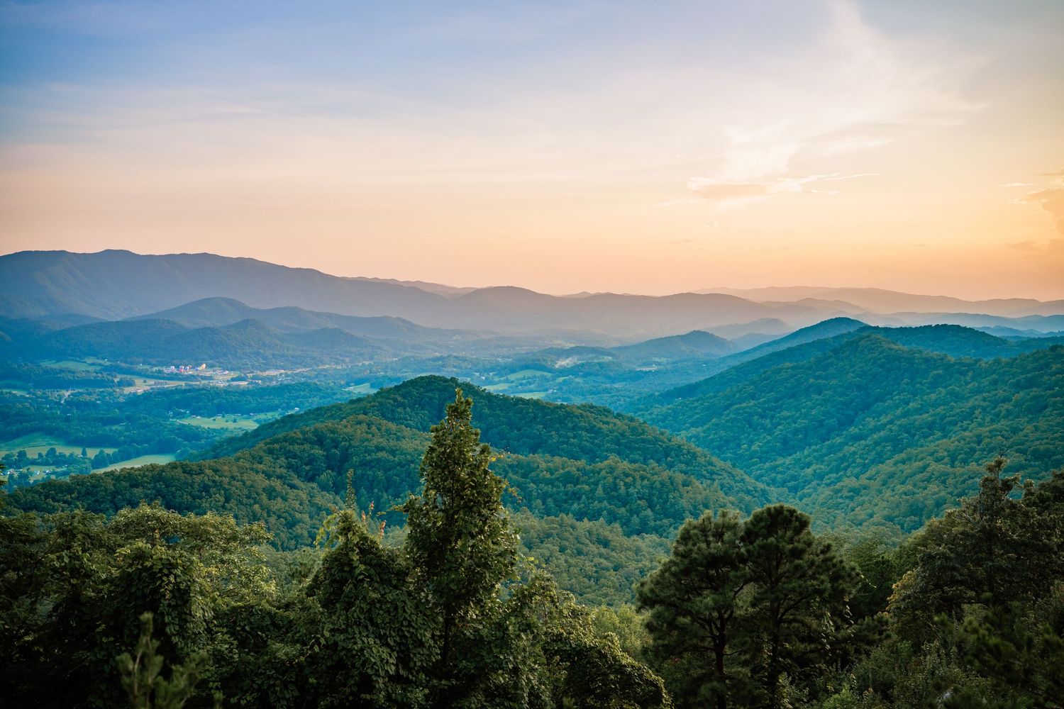 Panoramic sunset view over rolling Blue Ridge Mountain ranges covered in lush green forest trees.