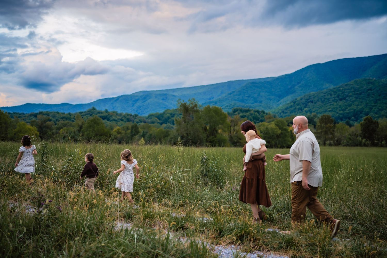 Family walking through green meadow with stunning Blue Ridge Mountain backdrop at dusk.
