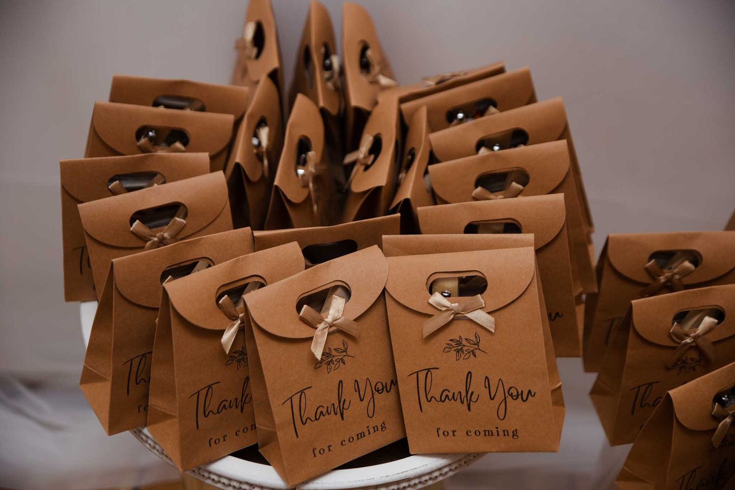 Kraft paper thank you wedding favor bags with ribbon ties displayed on a white table.
