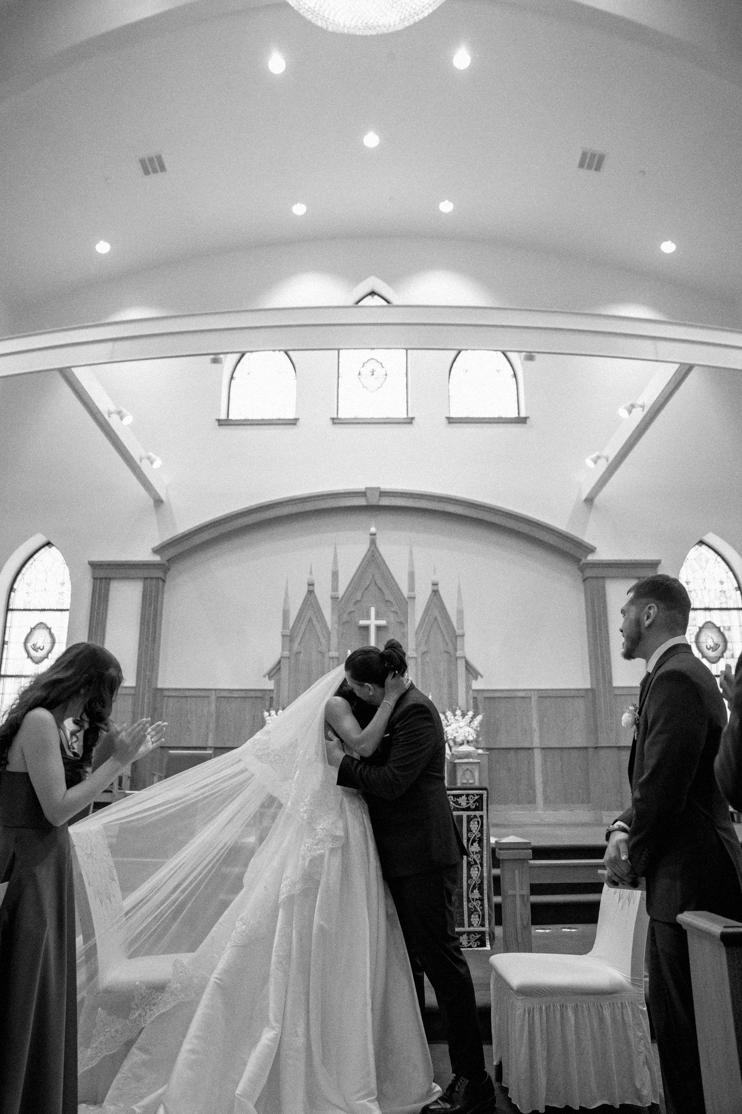 Black and white photo of a bride and groom sharing their first kiss at the altar in a beautiful church.
