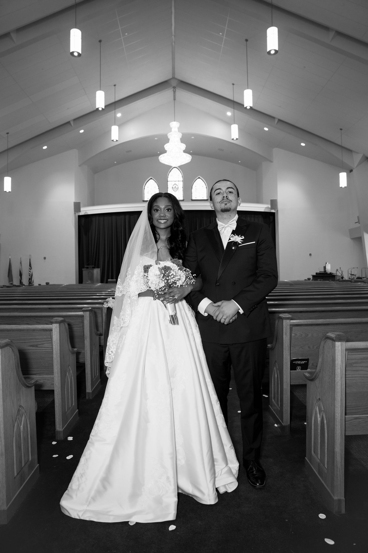 Black and white photo of a bride and groom walking down the aisle of a church after their wedding ceremony.