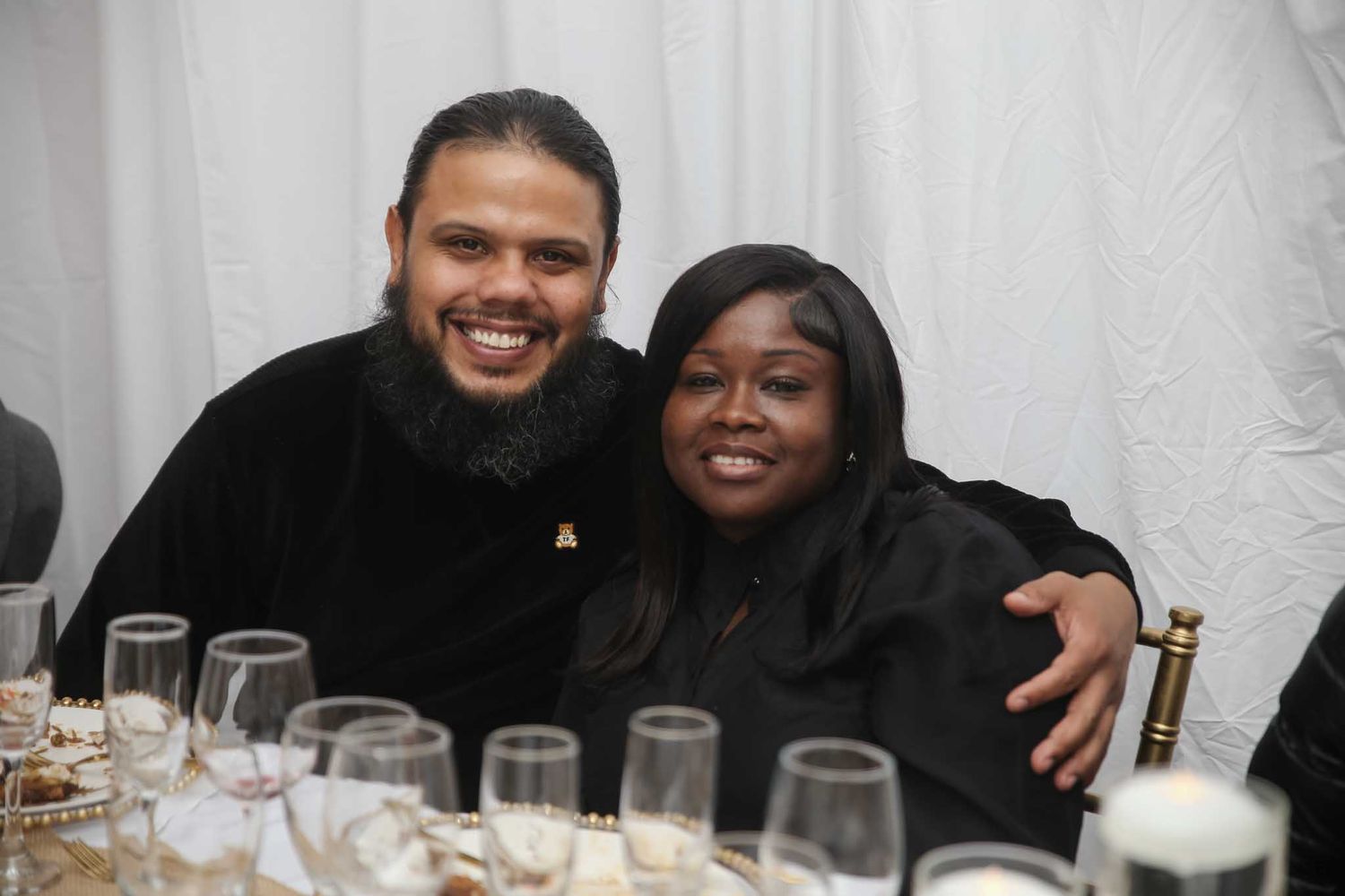 Smiling couple posing together at an elegant dinner event with glassware on the table.