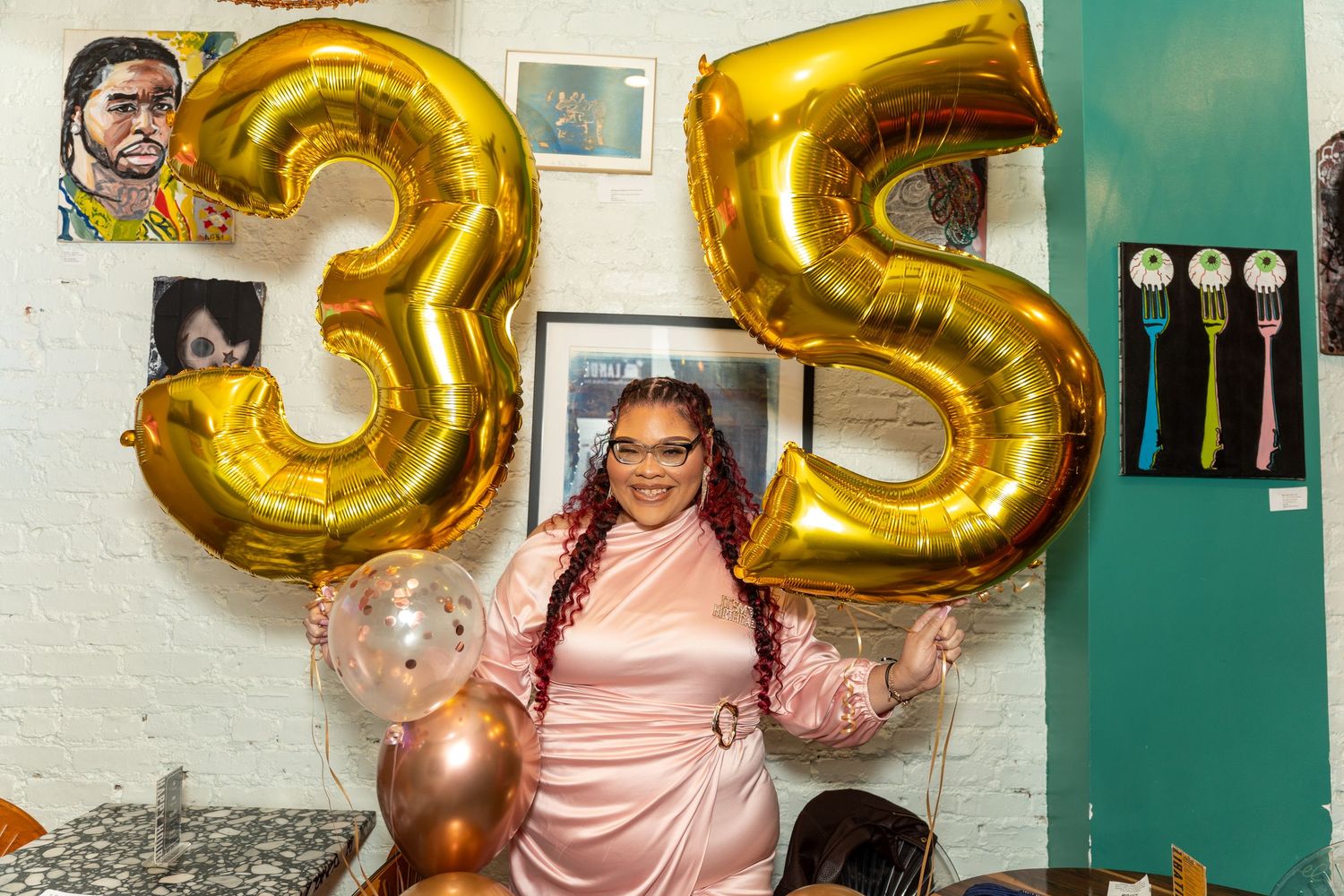 Woman holding gold number 35 balloons in pink satin dress at birthday celebration.