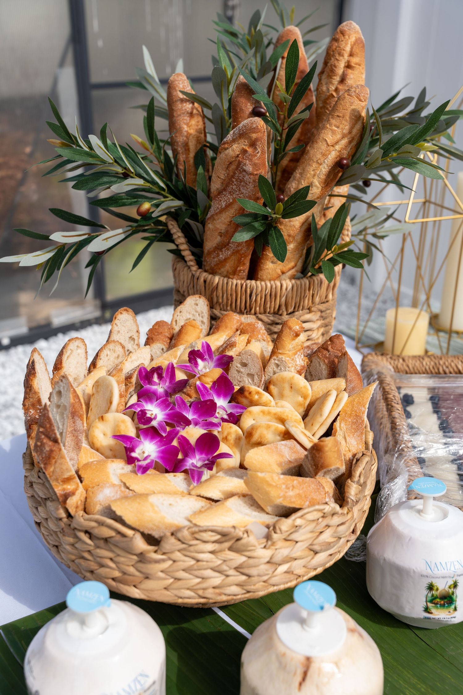 Wicker basket filled with French baguettes and sliced bread garnished with purple orchids and greenery.