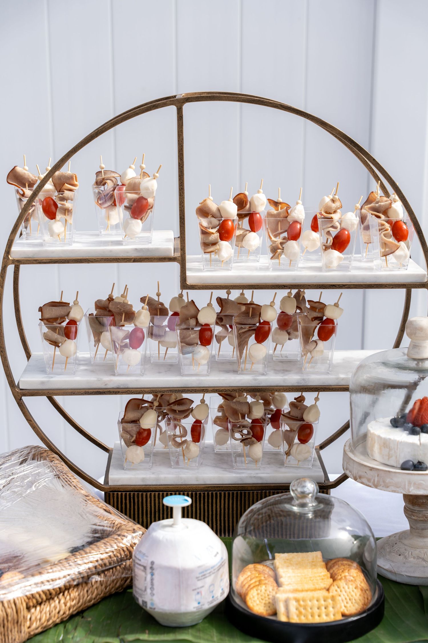 Elegant circular gold tiered display stand with charcuterie skewers, crackers, and appetizers.