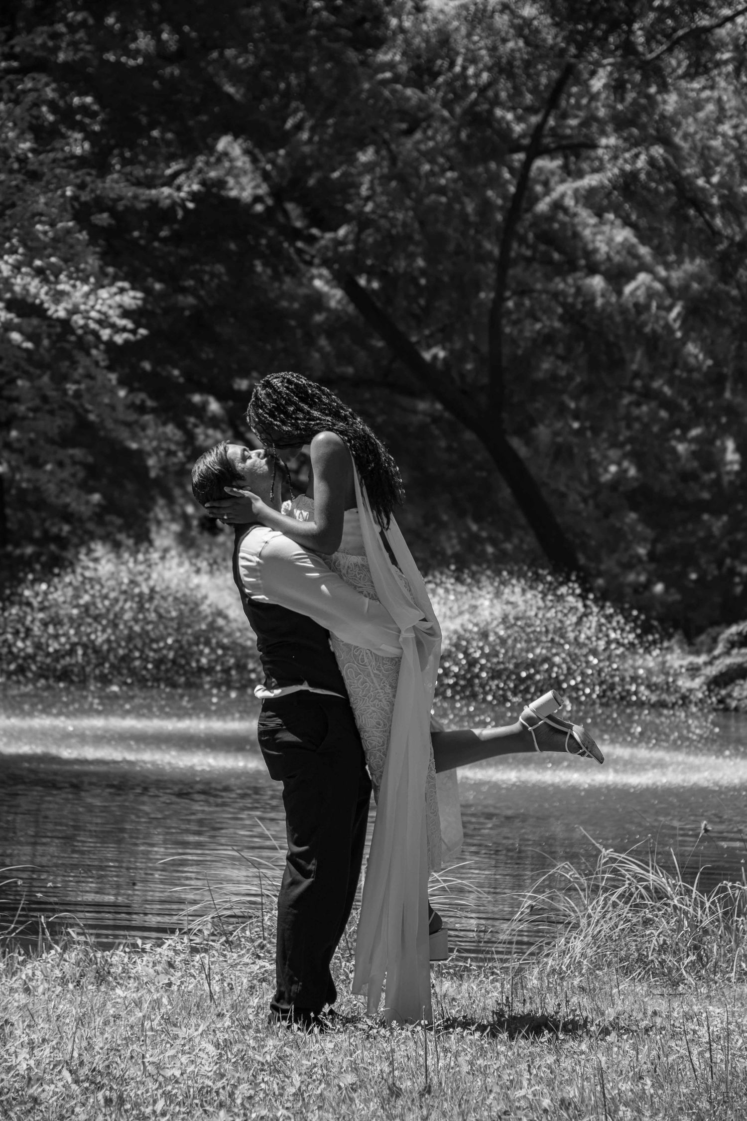 A black and white photo of a bride and groom sharing a romantic lift kiss near a serene lake.