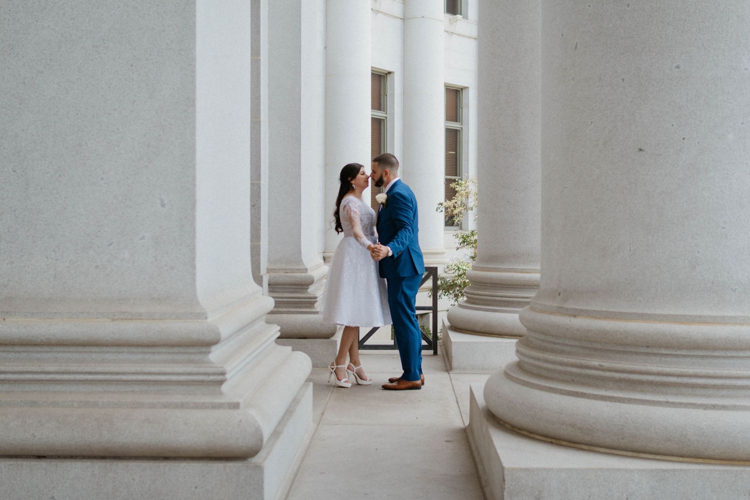 Couple sharing a romantic moment between grand white columns at an elegant building during their wedding day.