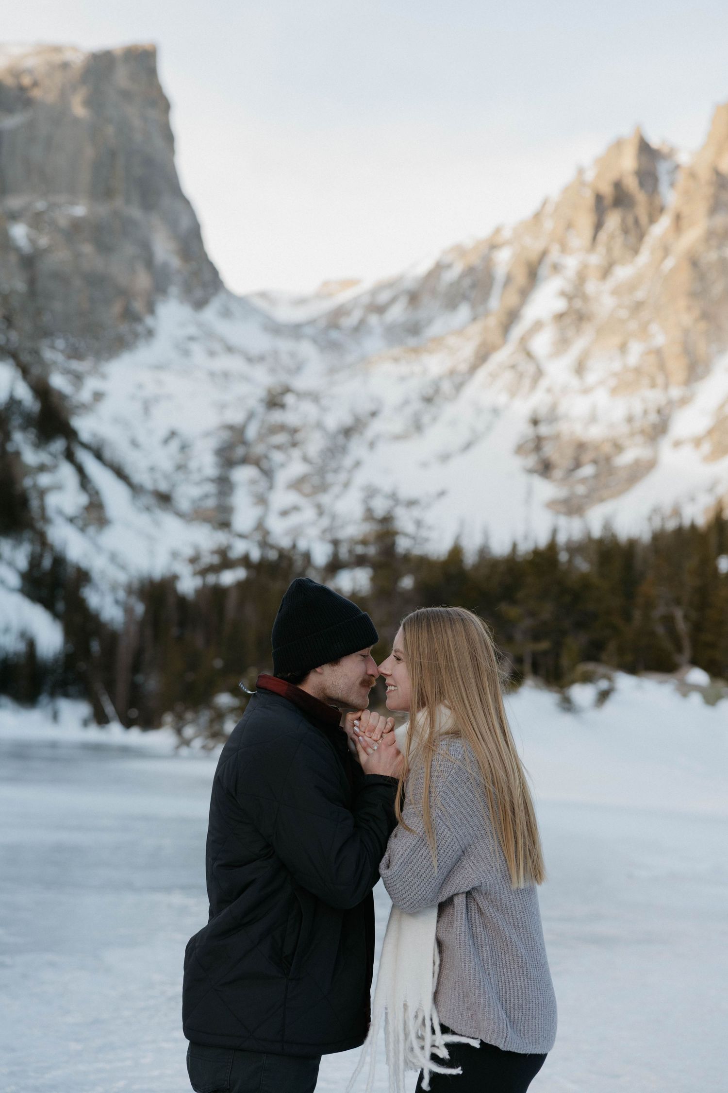 Couple sharing a romantic moment in front of a snow-covered mountain lake in winter.