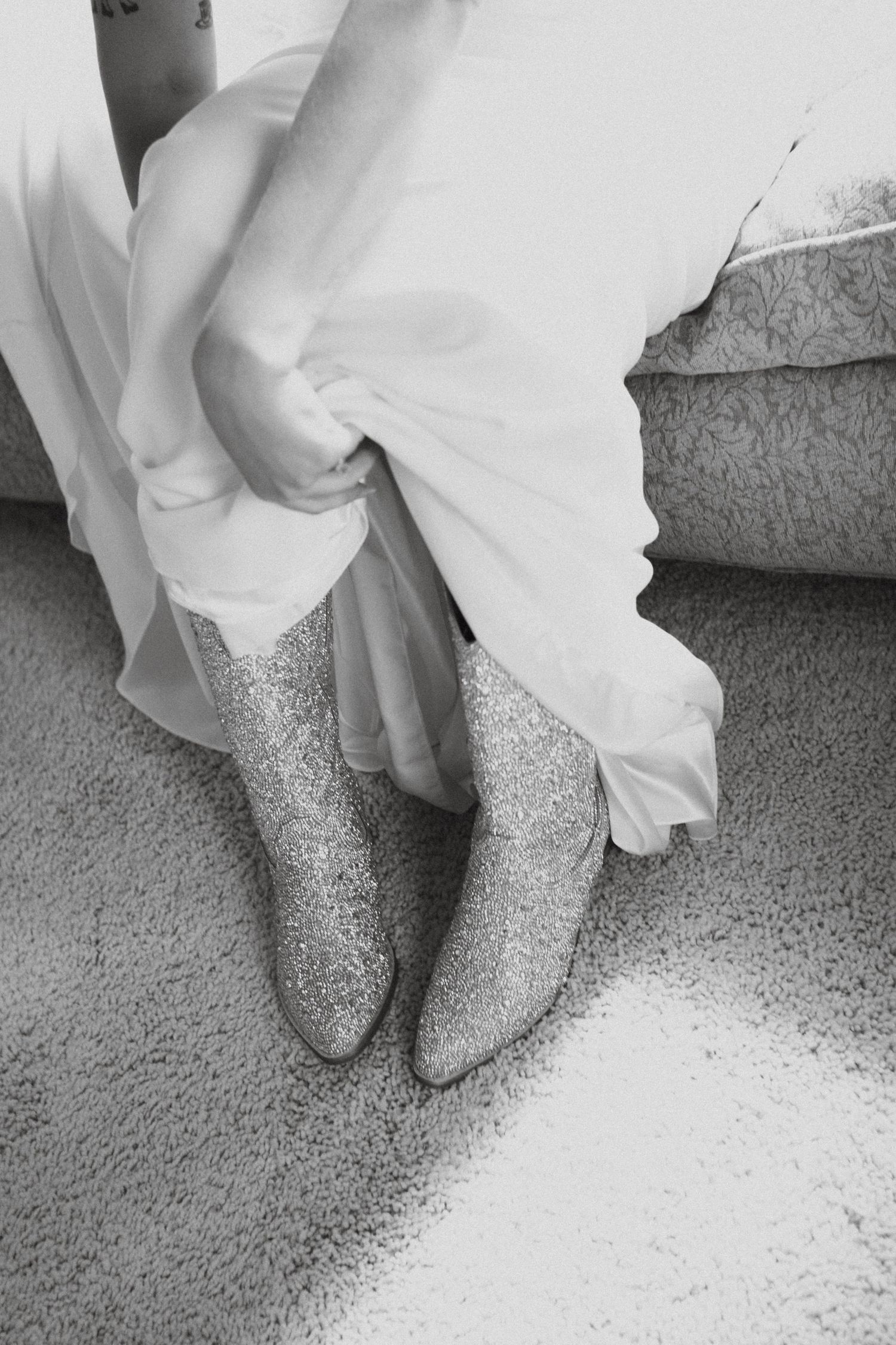 Black and white photo of a bride wearing glittery cowboy boots beneath her white wedding dress.