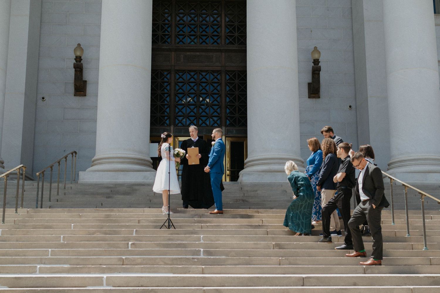 Wedding ceremony on grand building steps with bride, groom, and guests gathered outdoors.