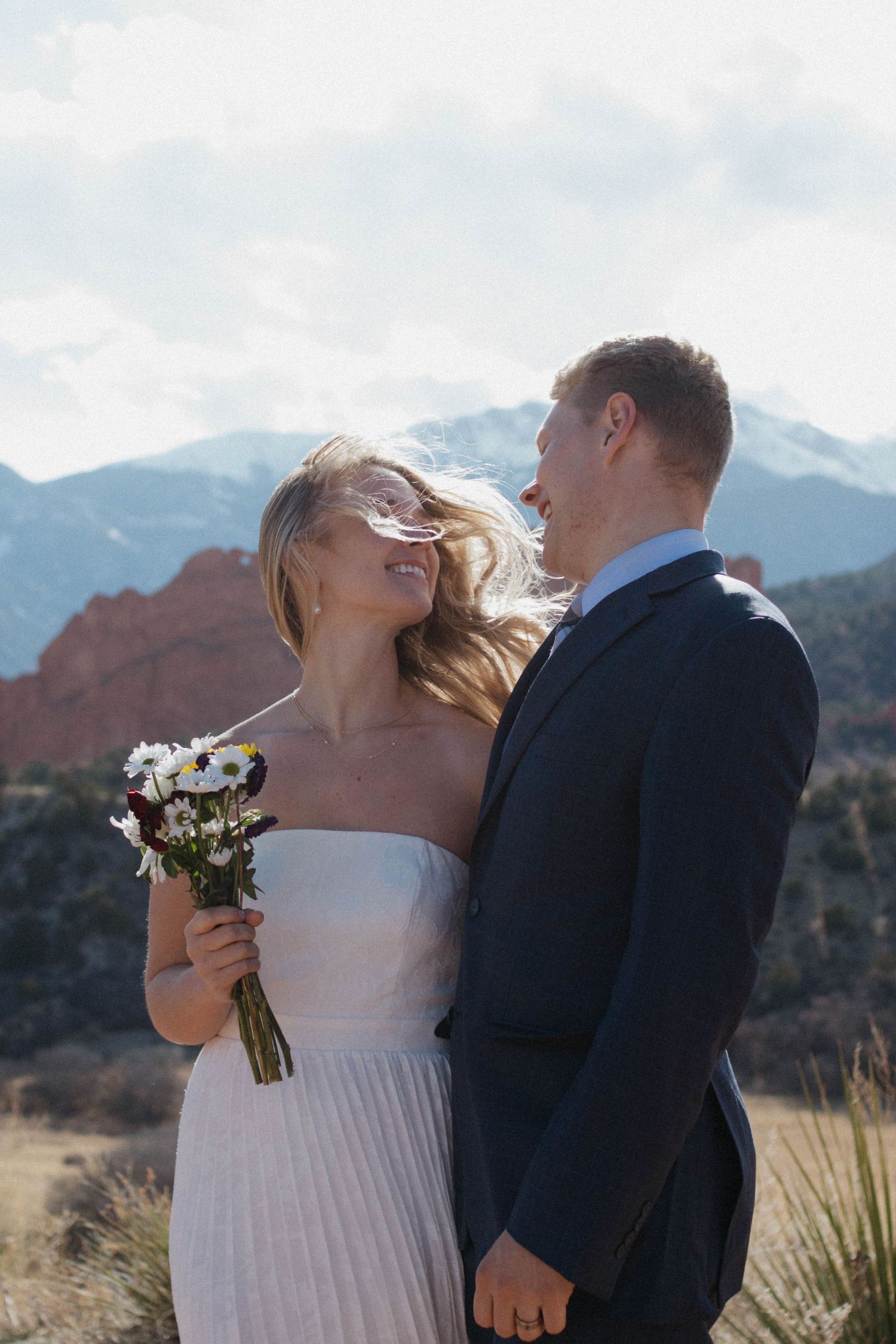 Bride and groom share a romantic moment at Garden of the Gods, Colorado, with red rocks and mountains backdrop.