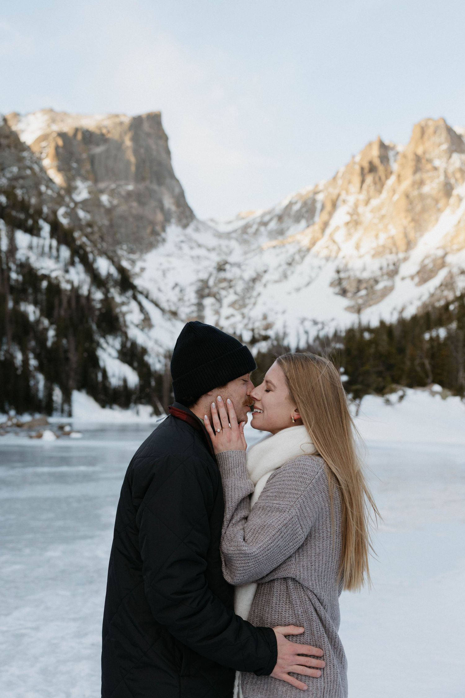 Couple sharing a romantic moment in front of a frozen lake and snow-capped mountains in winter.