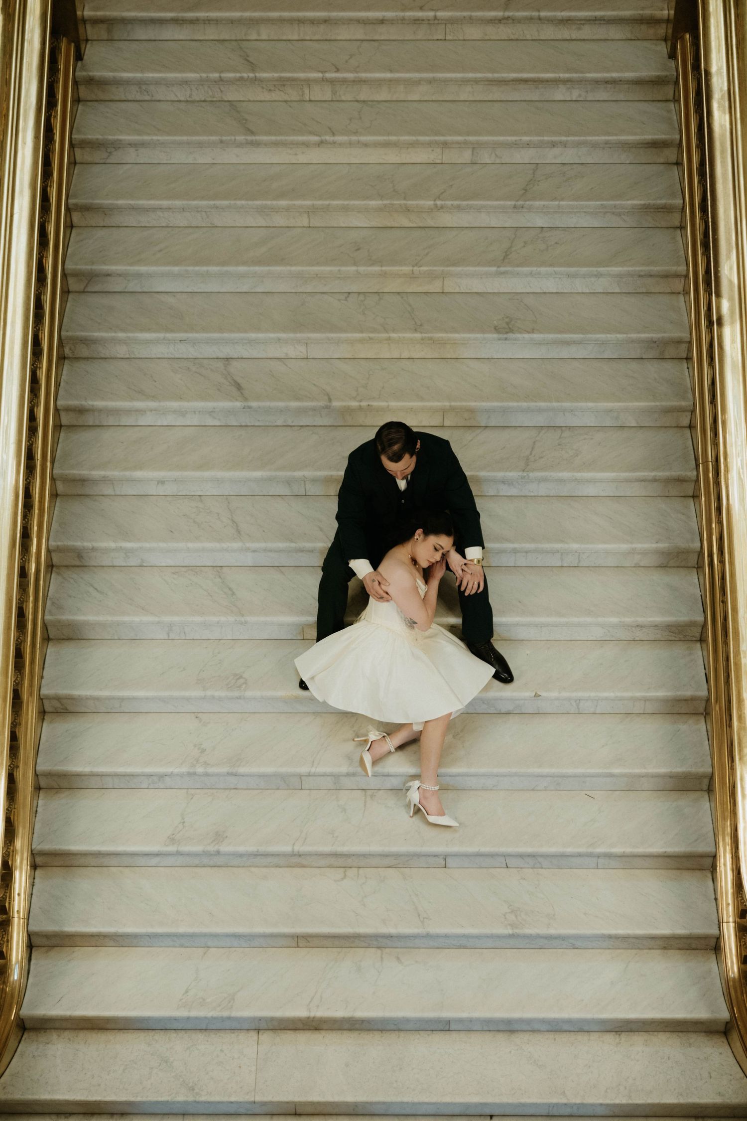 Aerial view of a couple embracing on marble stairs, bride in white dress and groom in black suit.