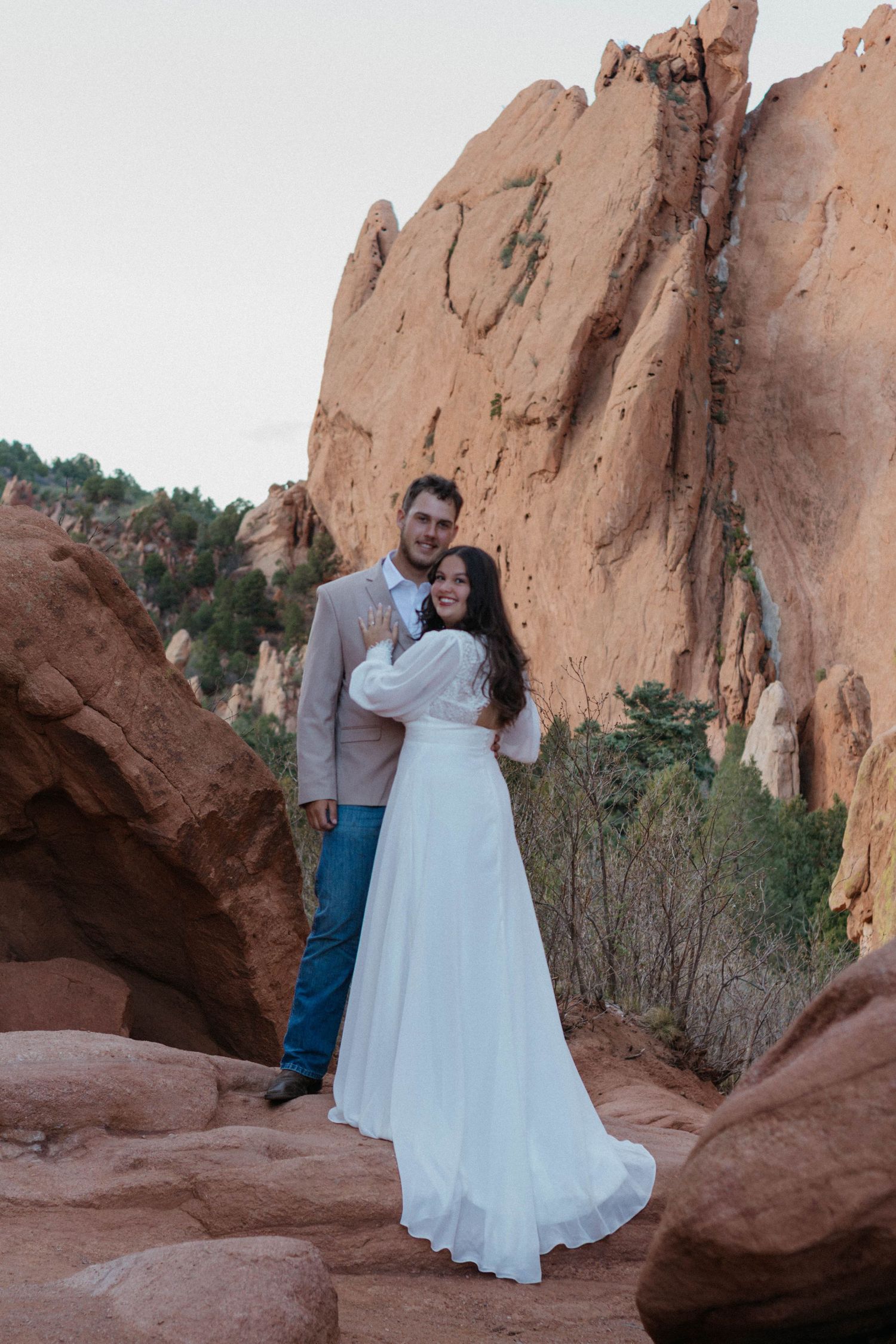 Couple in wedding attire posing among red rock formations at Garden of the Gods, Colorado.