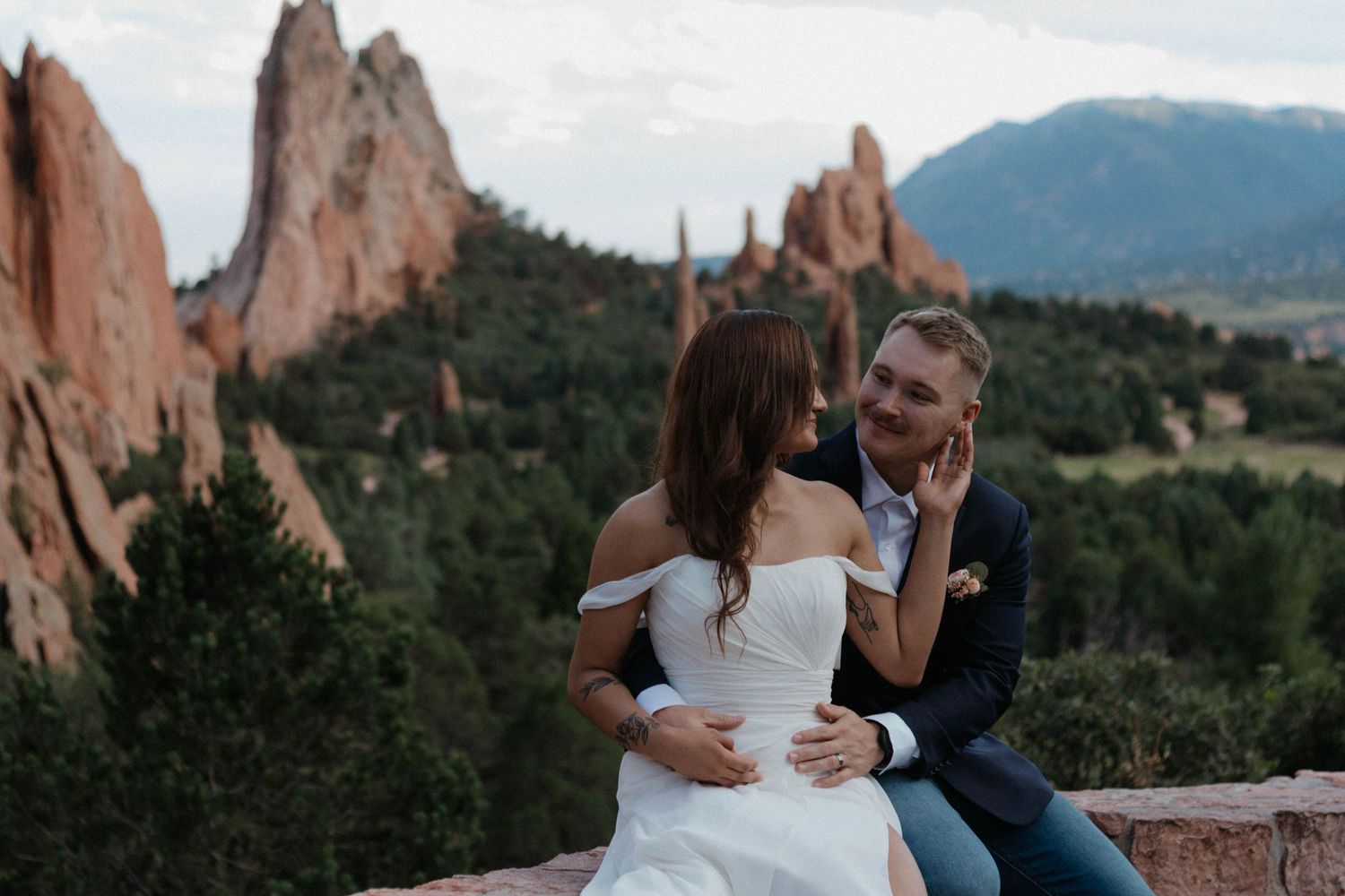 Bride and groom share a romantic moment at Garden of the Gods, Colorado, with red rock formations in the background.