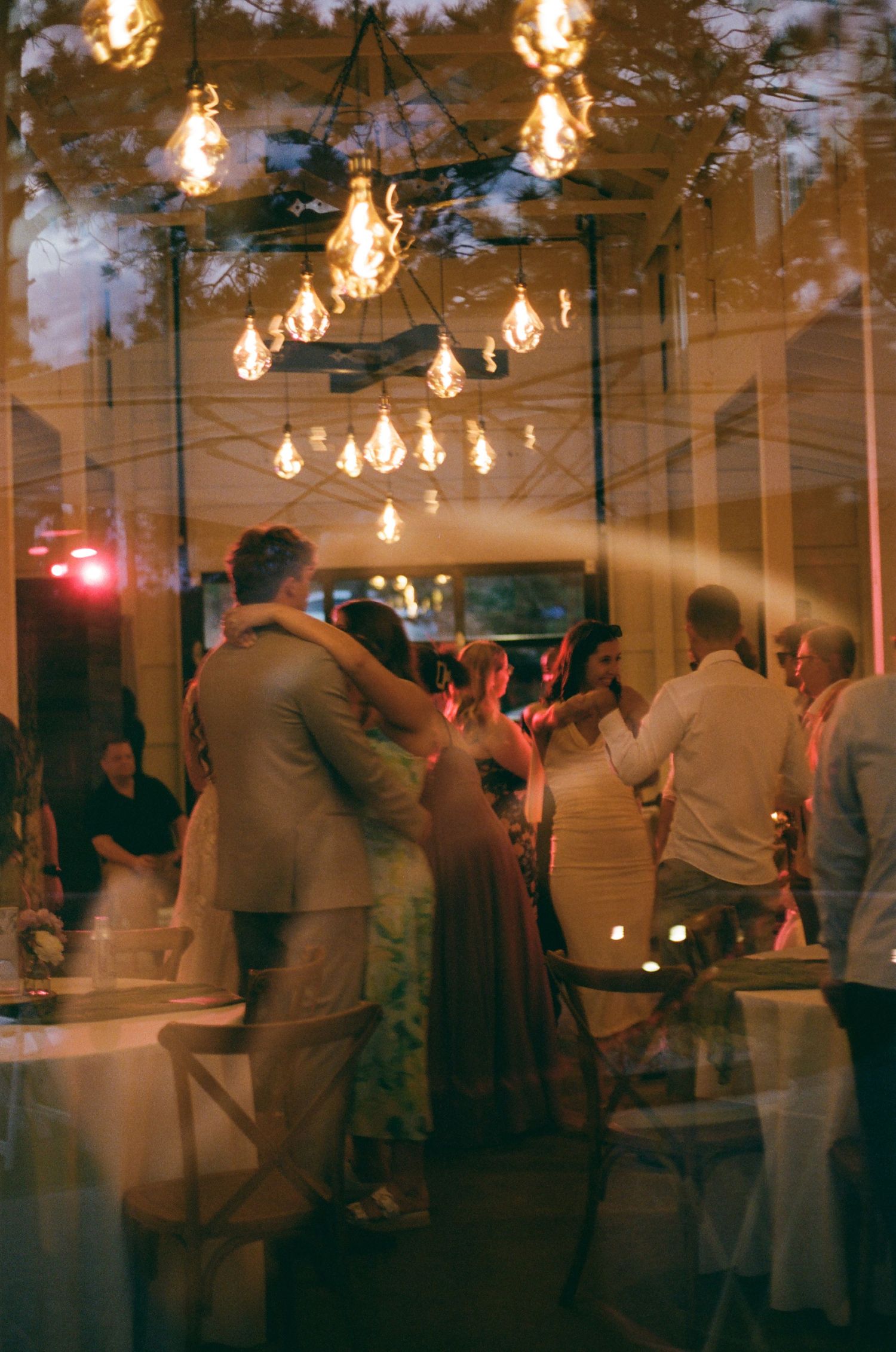 Couples dancing under warm Edison bulb lights at an elegant evening wedding reception party.