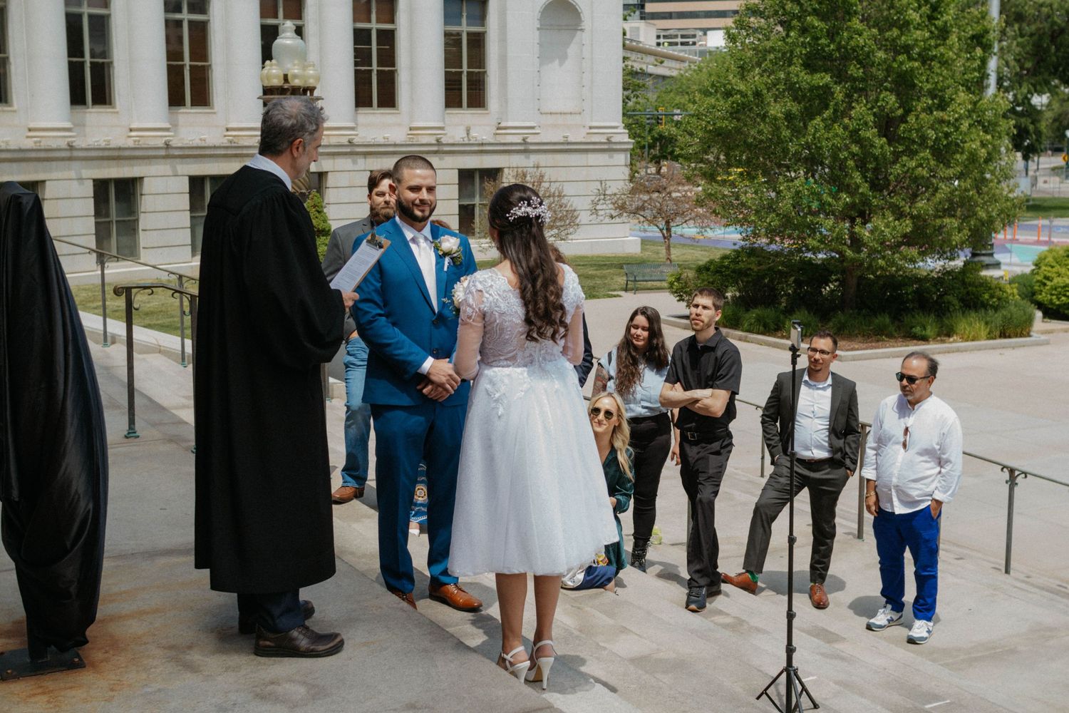 Outdoor wedding ceremony on courthouse steps with couple exchanging vows before officiant and guests.
