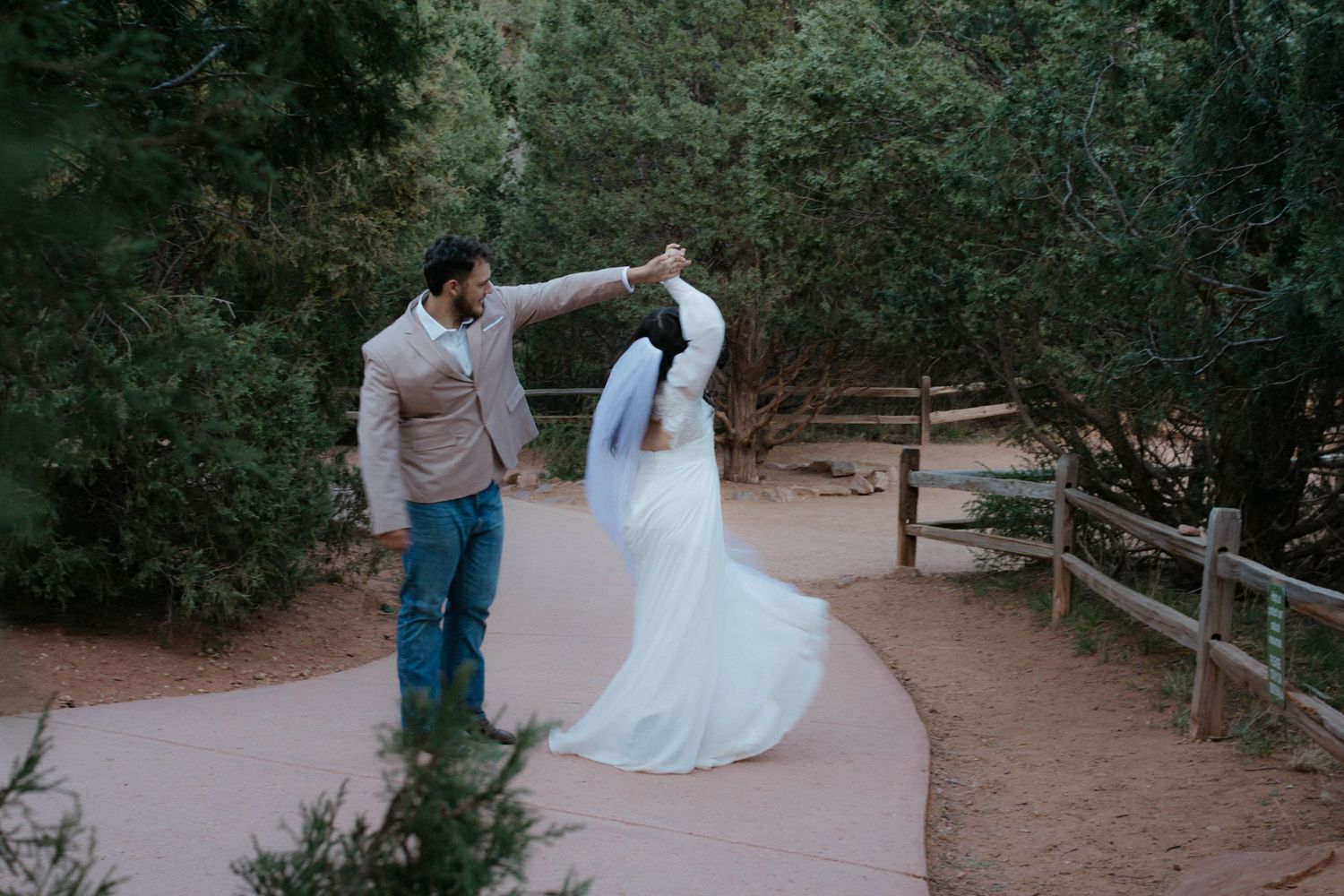 Bride and groom dancing on a sandy path surrounded by lush green trees in an outdoor wedding setting.