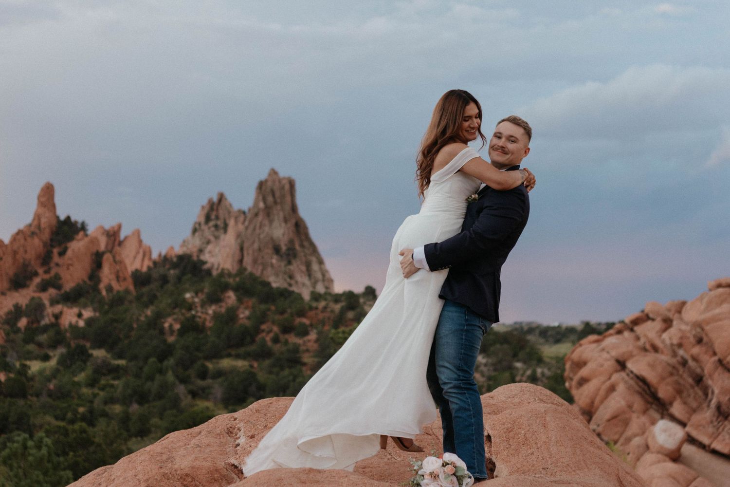 Couple in wedding attire embracing on red rocks at Garden of the Gods, Colorado, at sunset.