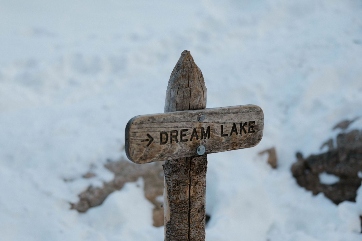 Rustic wooden directional sign pointing to Dream Lake covered in snow in a winter landscape.