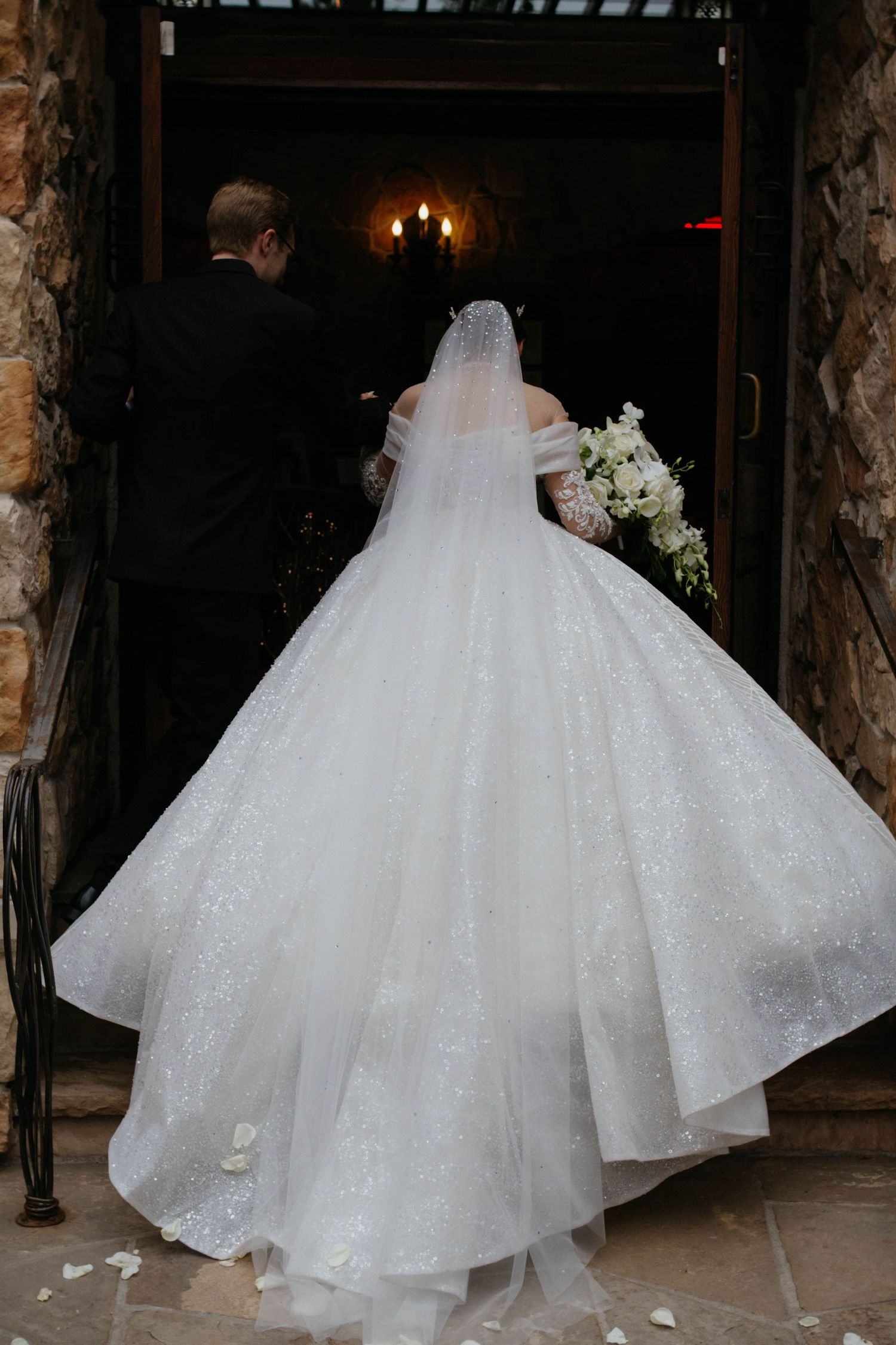A bride in a flowing white ball gown with a cathedral train walks through a dimly lit venue during her wedding.