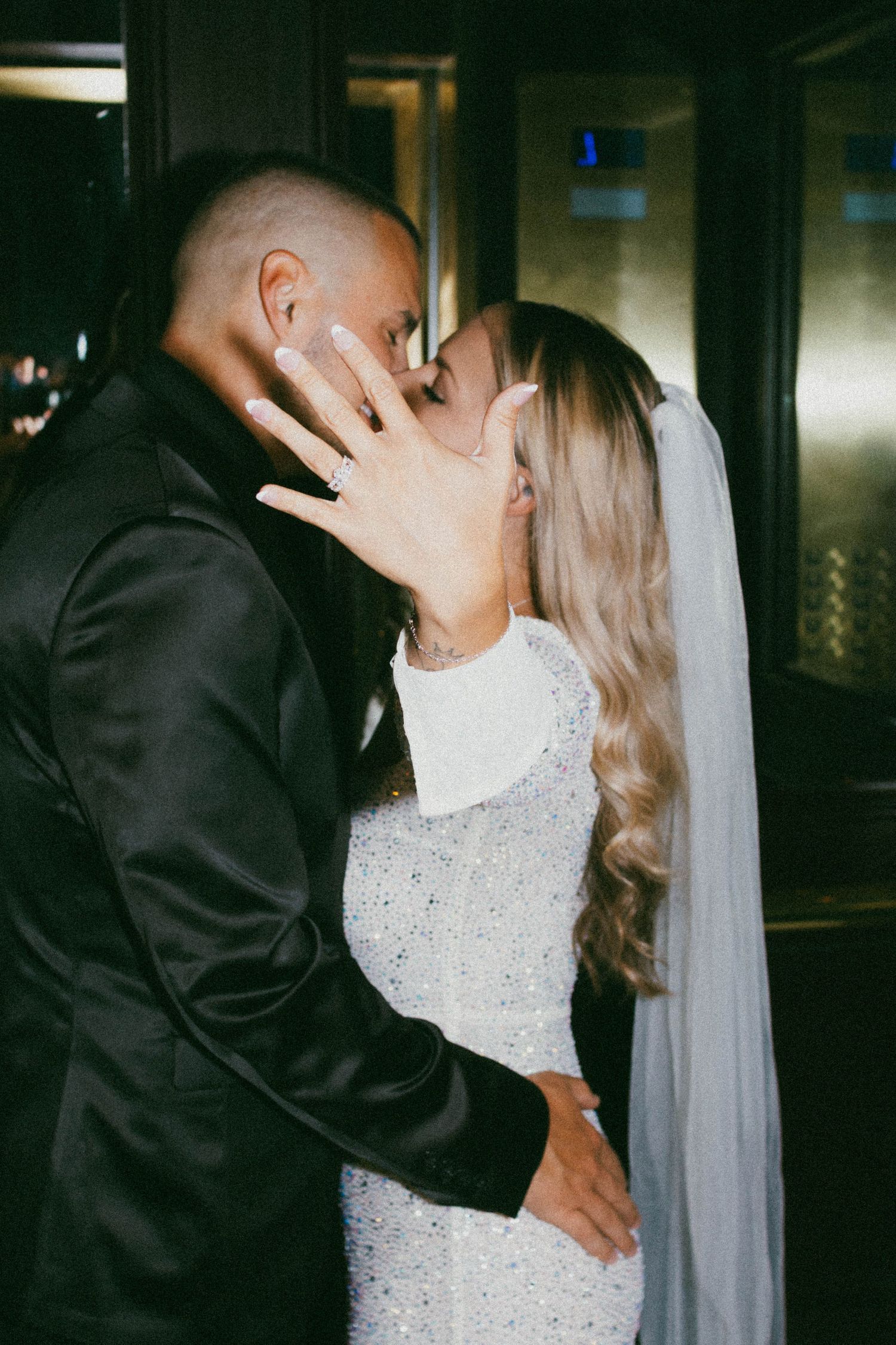 A romantic wedding moment showing a couple in black and white attire sharing a tender kiss with a flowing veil.
