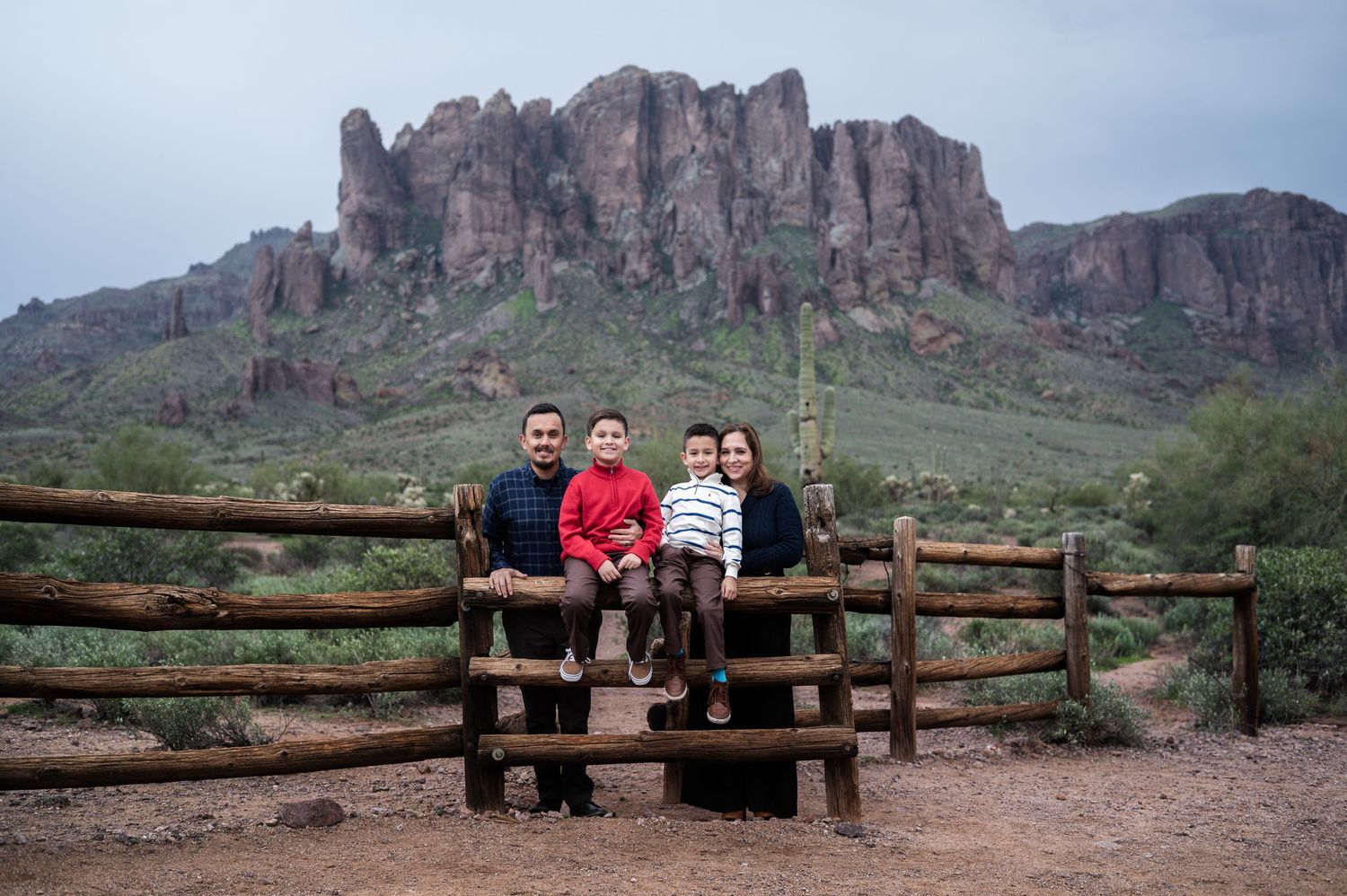 Family of four posing on a bench with Superstition Mountains in the Arizona desert background.