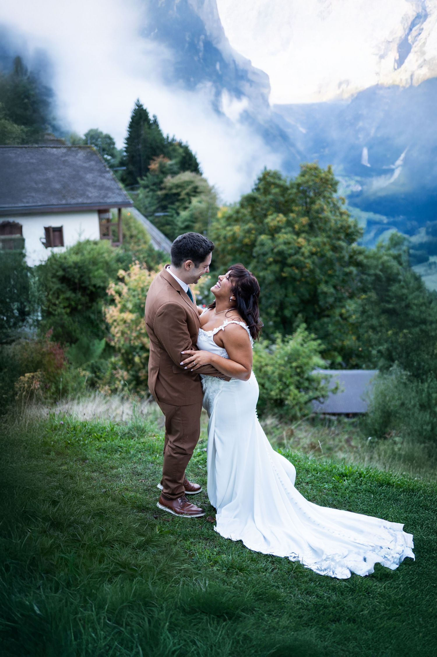 Bride and groom embracing in a lush green valley with misty mountains and waterfall in background in Wengen Switzerland on their elopement.