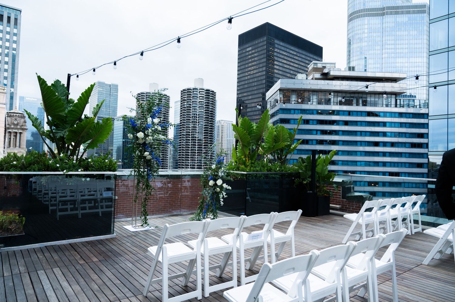 Elegant rooftop wedding ceremony setup with white chairs, floral arch, and city skyline backdrop at The Pendry Hotel in Chicago Illinois.