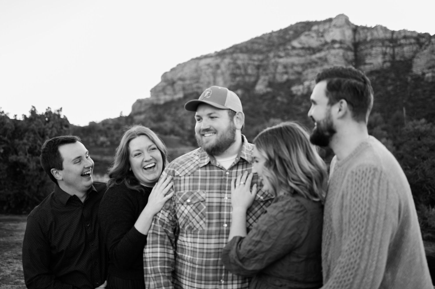 Black and white candid family photo with five adults laughing together against Sedona red rock backdrop.