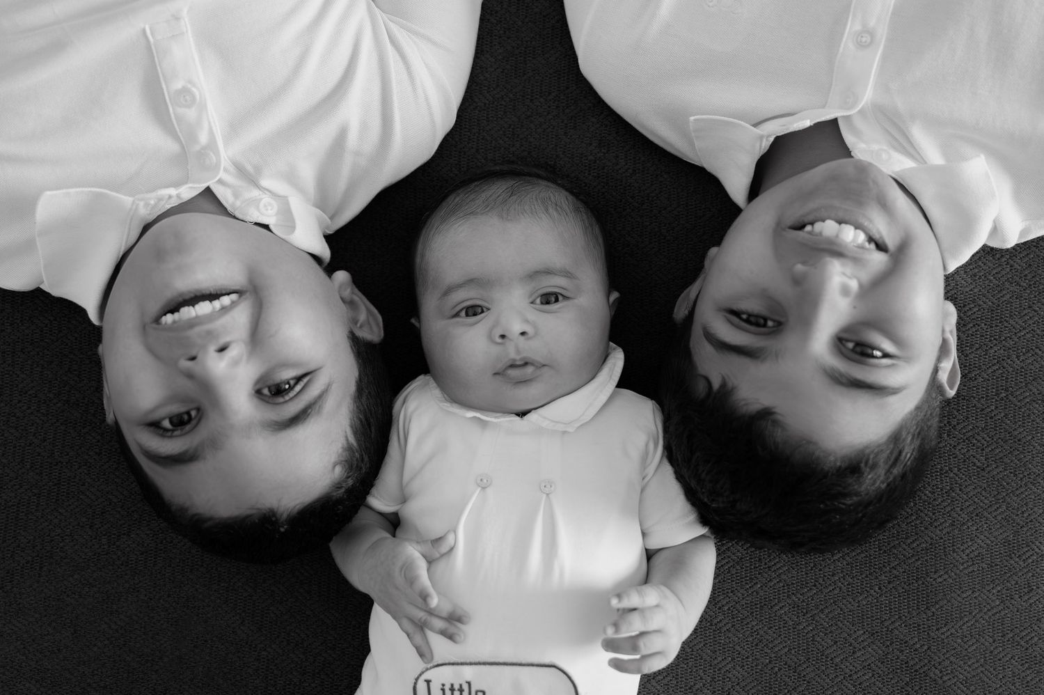 Black and white overhead portrait of three siblings and newborn baby lying on floor together in an in home family session in Jubail saudi