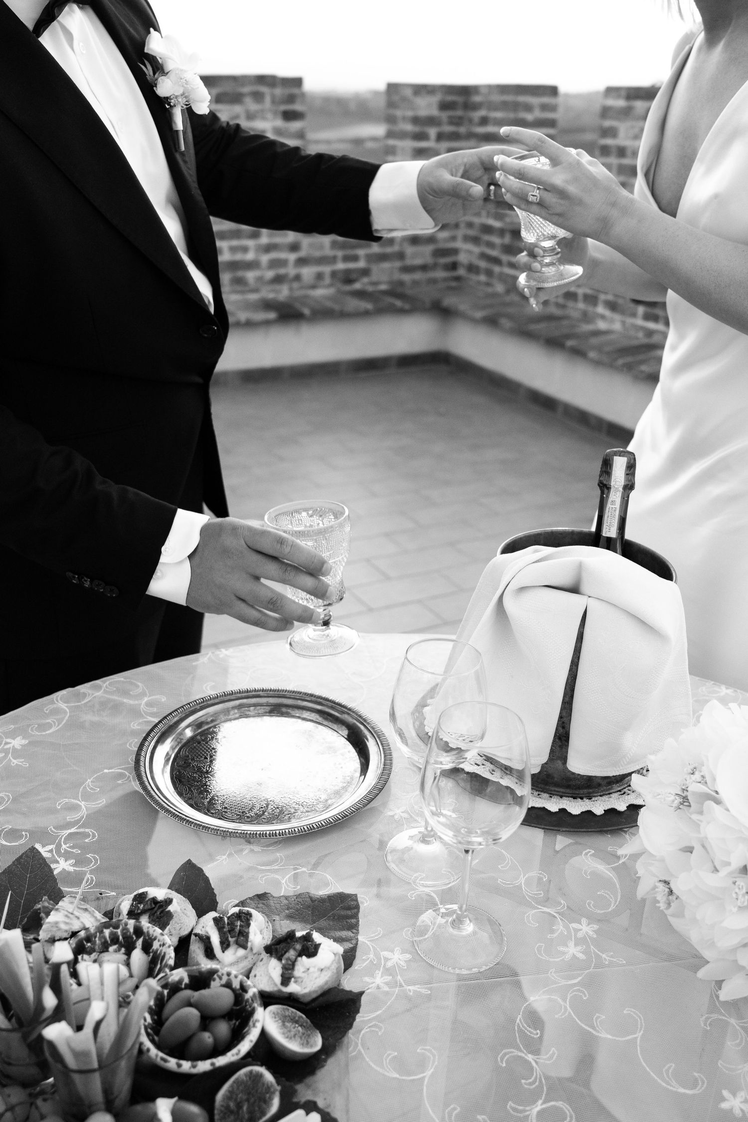 Black and white photo of bride and groom toasting champagne at elegant outdoor wedding reception table in Tuscany Italy.