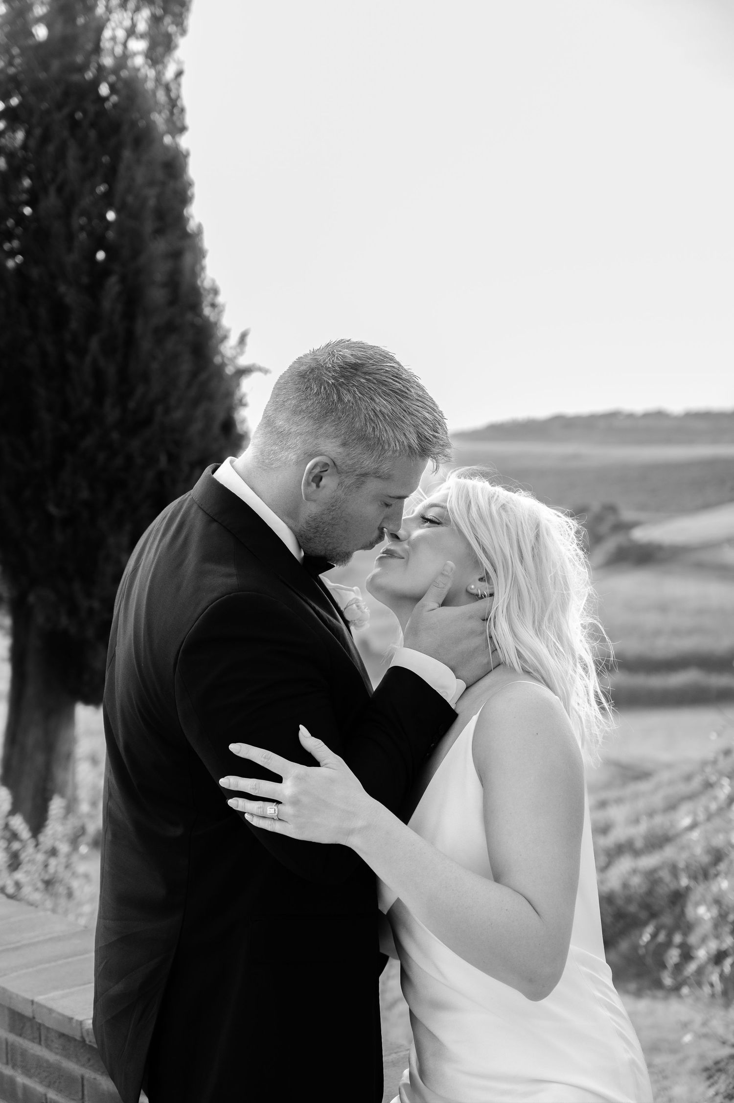 Black and white photo of blonde bride and groom sharing tender kiss at outdoor wedding venue in Tuscany Italy.