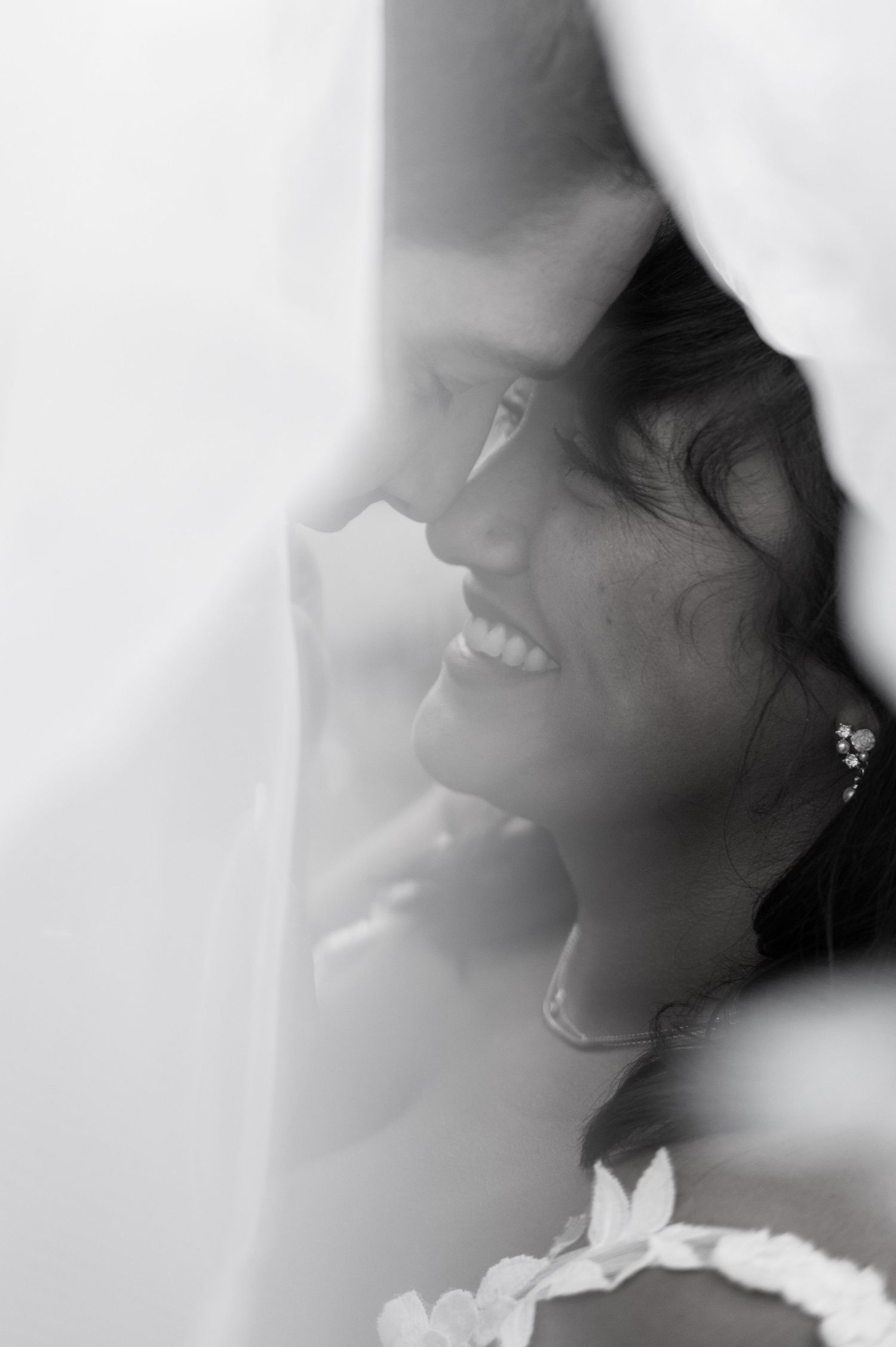 Close-up black and white portrait of a smiling bride partially veiled, wearing floral earrings in Lauterbrunnen Switzerland.