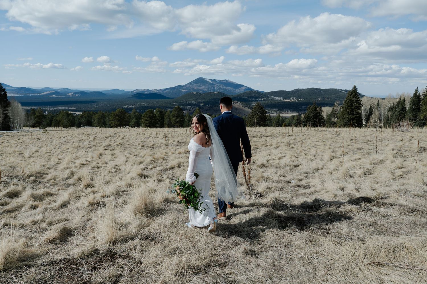 Bride and groom walk through open mountain meadow with scenic peaks in outdoor elopement photo In flagstaff.