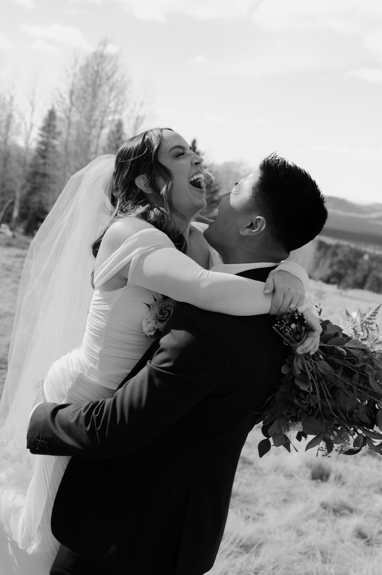 Black and white photo of joyful groom lifting laughing bride in wedding dress outdoors in arizona