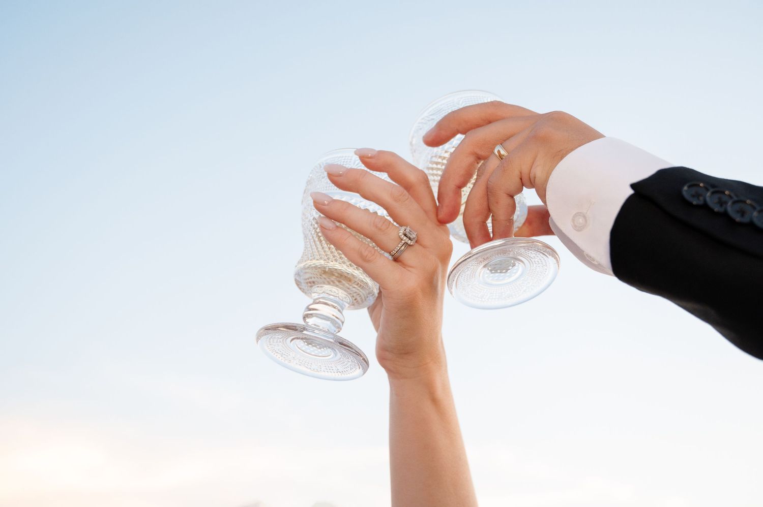 Bride and groom toasting with elegant crystal champagne glasses against a blue sky at their wedding in Tuscany Italy.