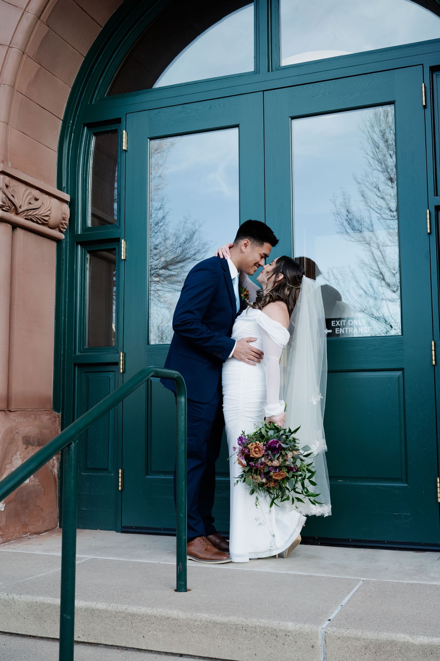 Bride and groom sharing a kiss on church steps with teal doors and colorful bouquet at the Flagstaff courthouse in Arizona.