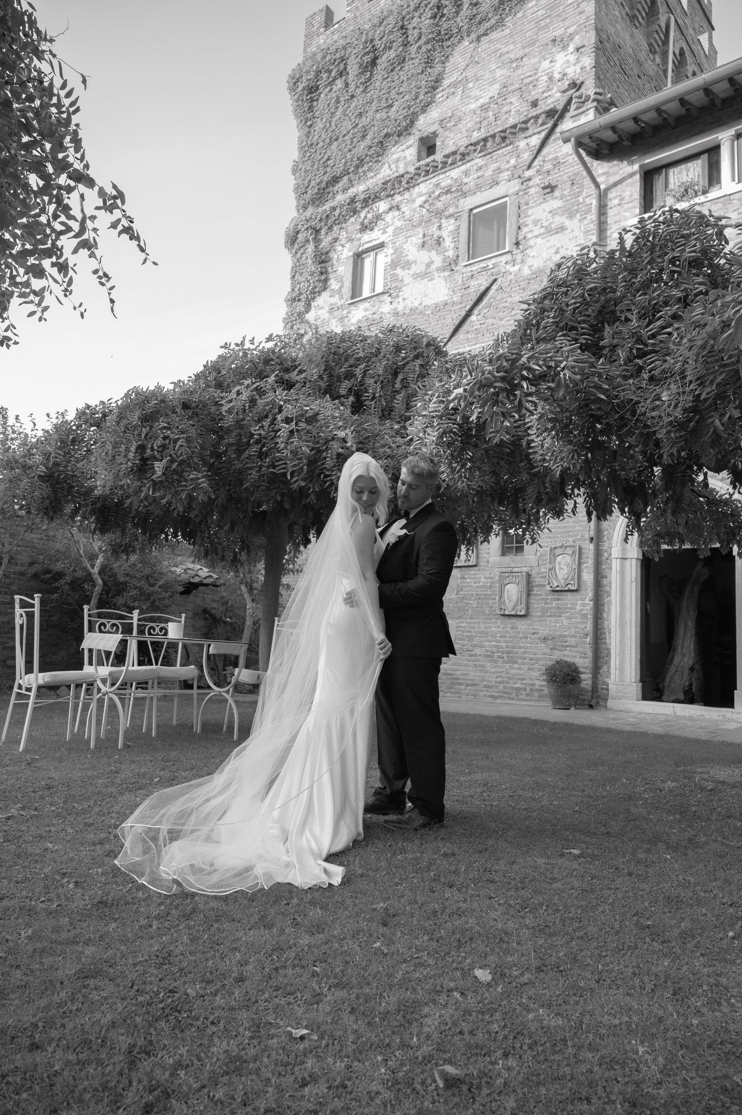 Bride and groom sharing a kiss in black and white portrait before a historic Tuscan castle in Tuscany Italy.