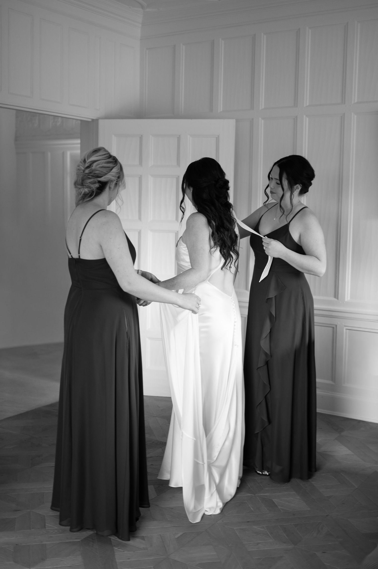 Bride in white gown assisted by two bridesmaids in dark dresses during wedding preparations at The Pendry Hotel in Chicago Illinois.