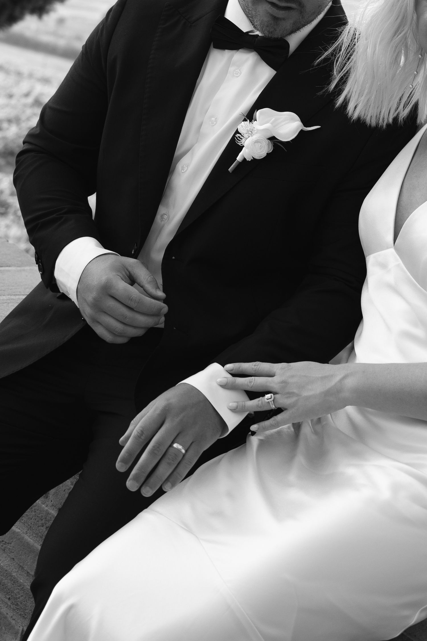 Black and white close-up of bride and groom sitting together, showcasing wedding ring and boutonniere details in Tuscany Italy.