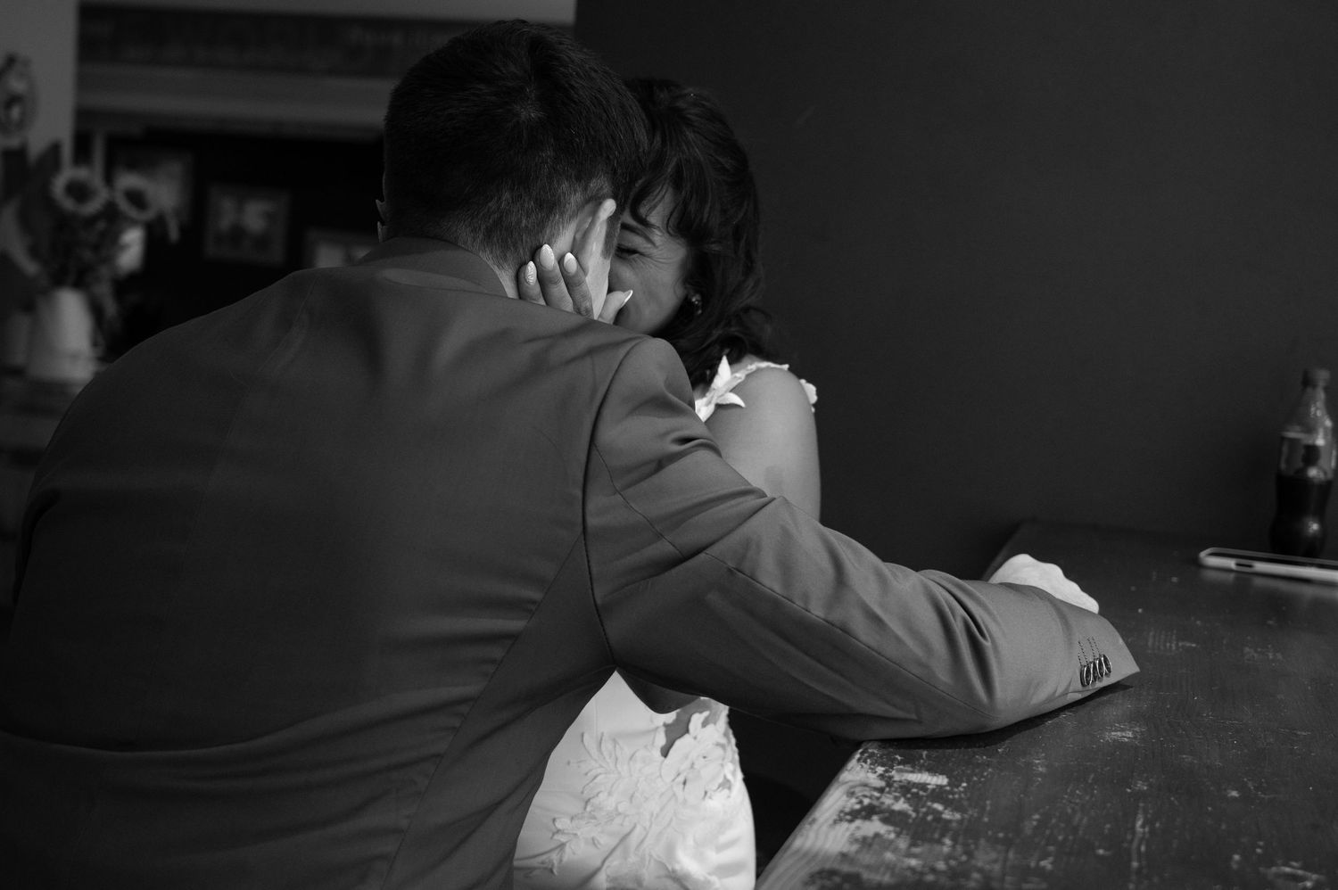 Black and white photo of bride and groom sharing quiet intimate moment at rustic bar.