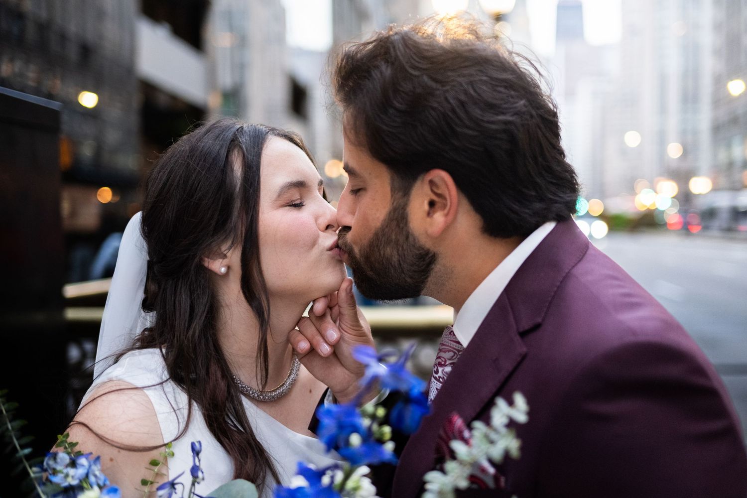 Bride and groom share a romantic kiss outdoors with blue and white wedding bouquet in foreground  at The Pendry Hotel in Chicago Illinois.