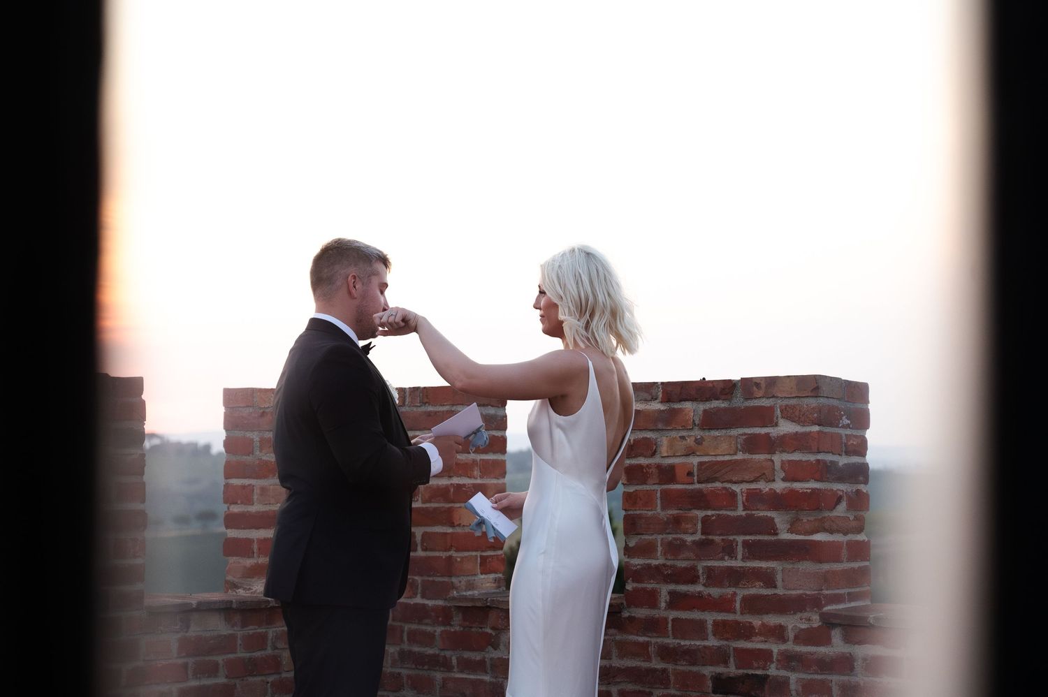 Bride and groom sharing tender moment on rustic brick rooftop terrace at golden hour wedding in Tuscany Italy.