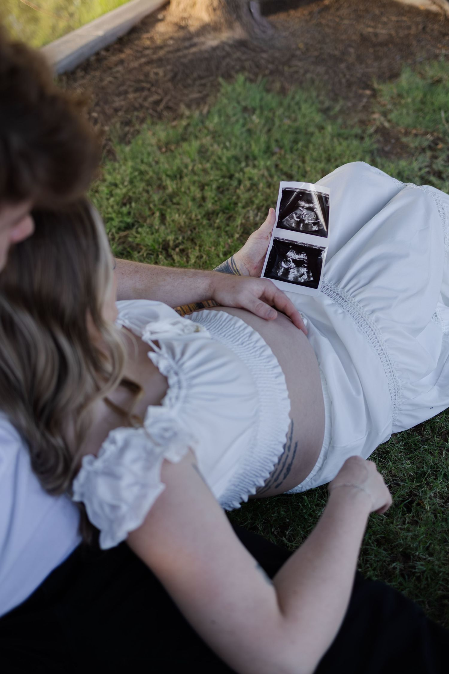 Overhead view of pregnant woman and partner looking at ultrasound photos on her baby bump outdoors in phoenix